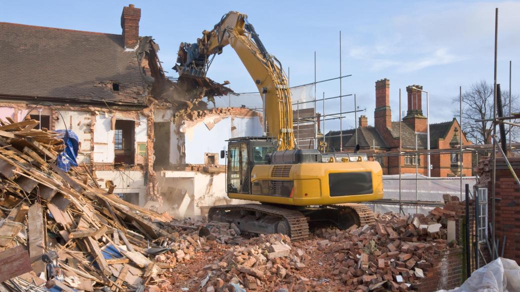 large tracked excavator machine fitted with a demolition tool, ripping apart old houses and buildings in a town centre for re-development.