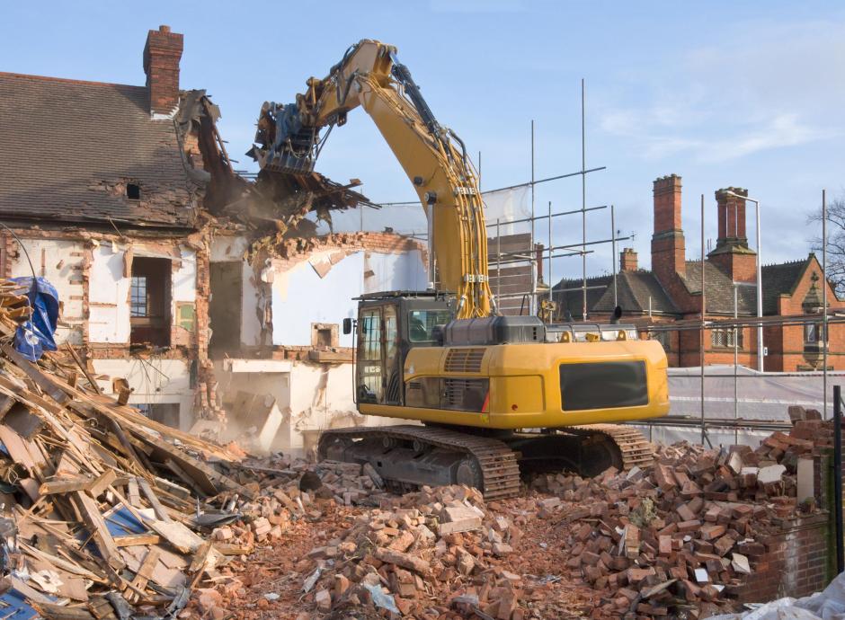 large tracked excavator machine fitted with a demolition tool, ripping apart old houses and buildings in a town centre for re-development.
